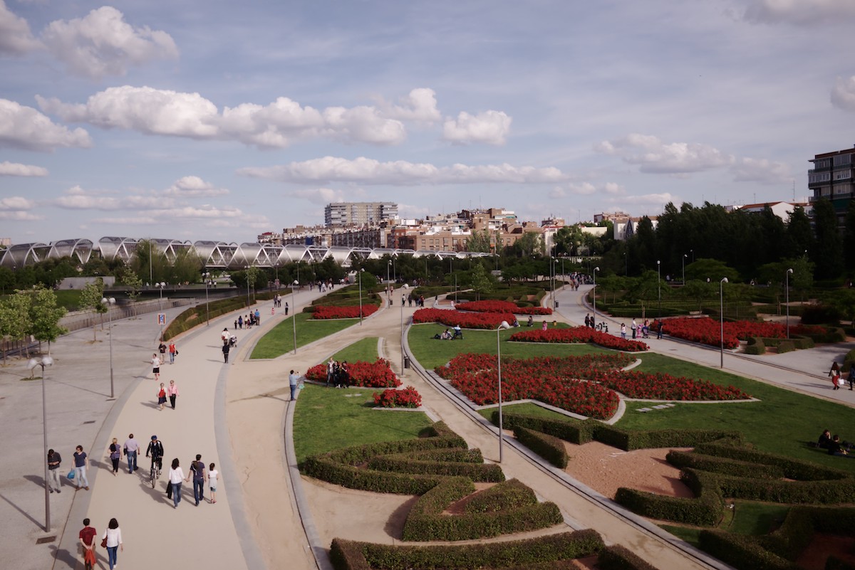 Walking paths and floral areas at Madrid Rio park, one of Madrid's hidden gems, with part of the city skyline visible in the background.