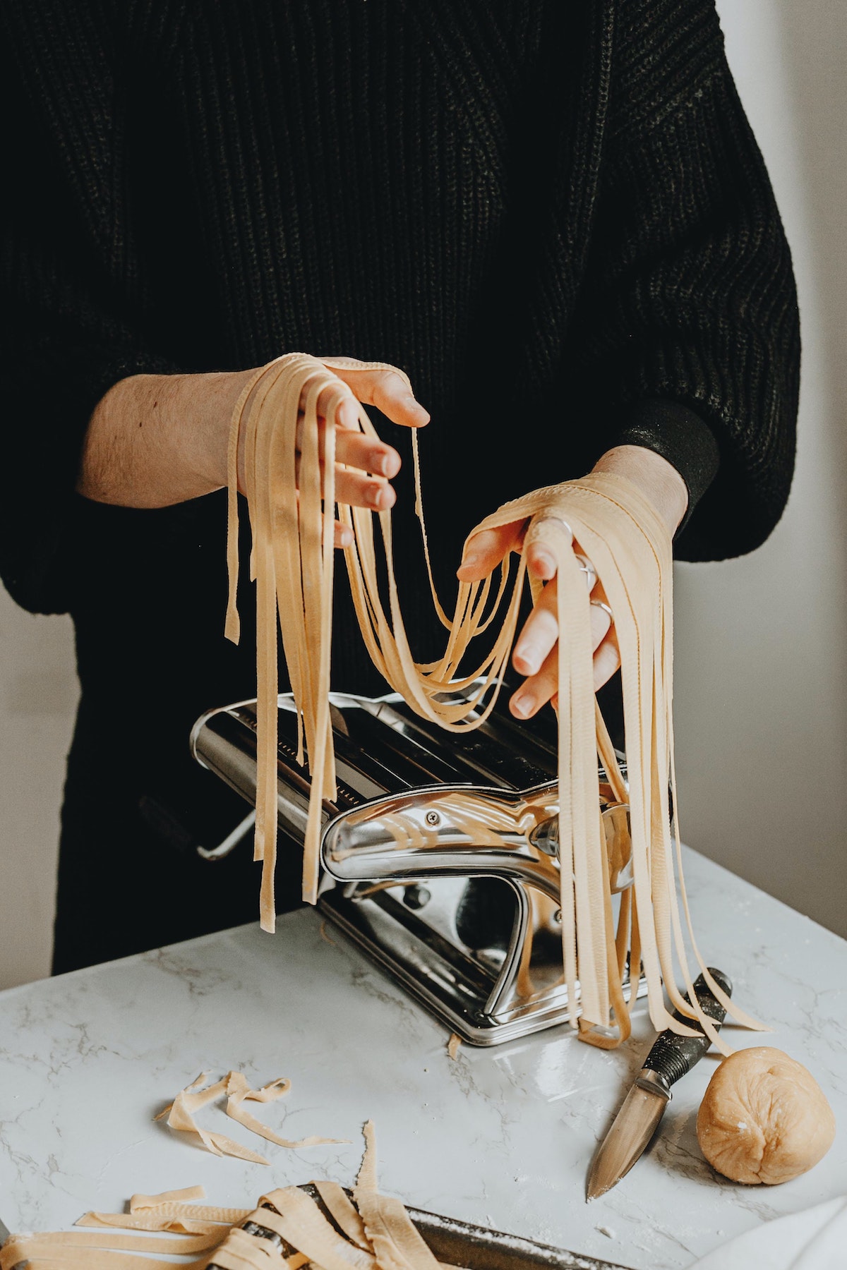 A person wearing a black shirt holding homemade fresh fettuccine noodles