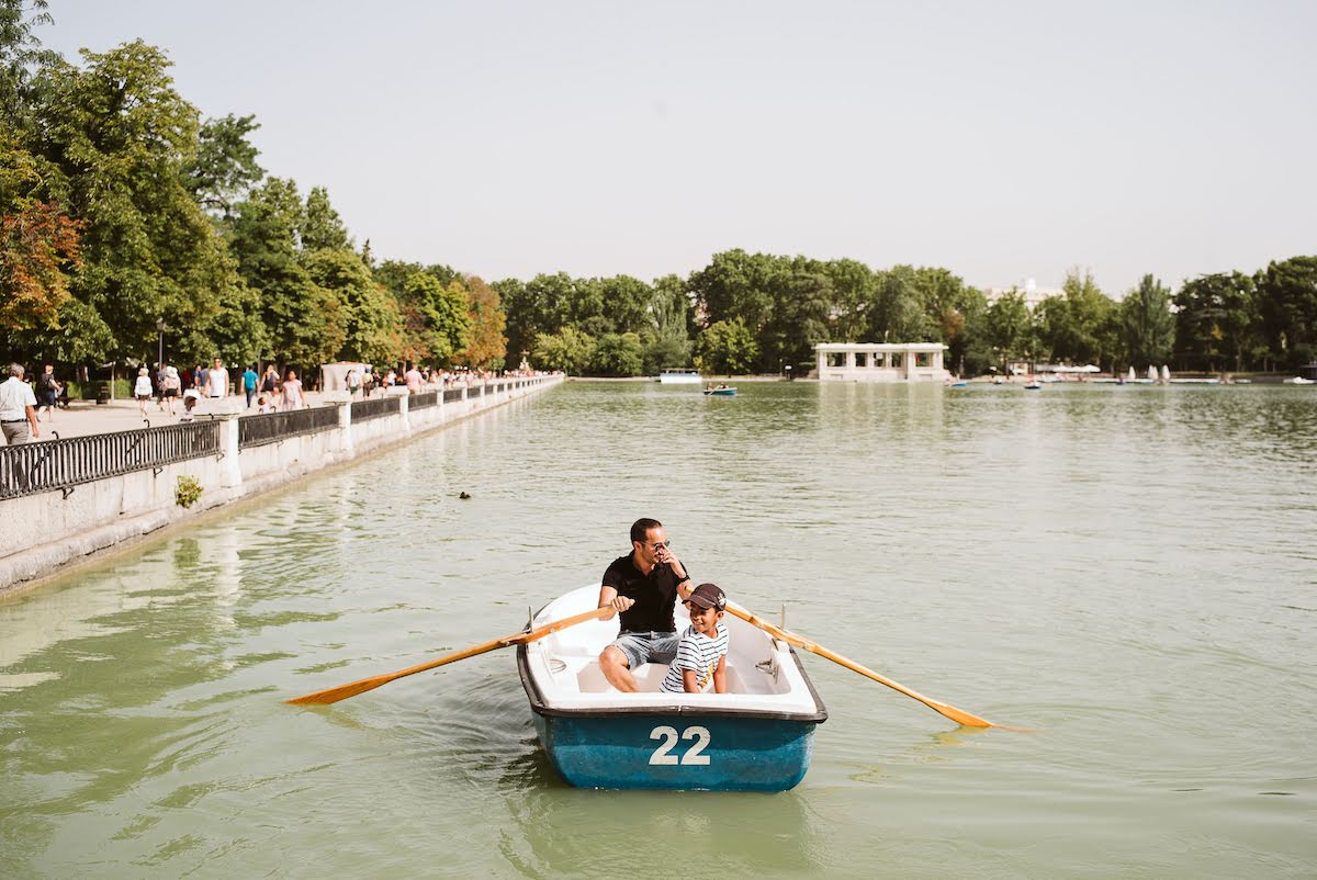 A father with his young son rowing a boat around a small lake.