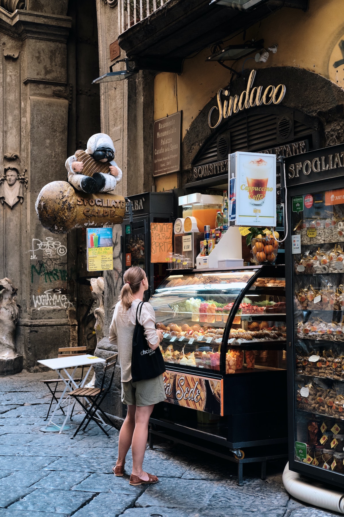 A woman stands on the street and looks inside a bakery display case in Naples, Italy.