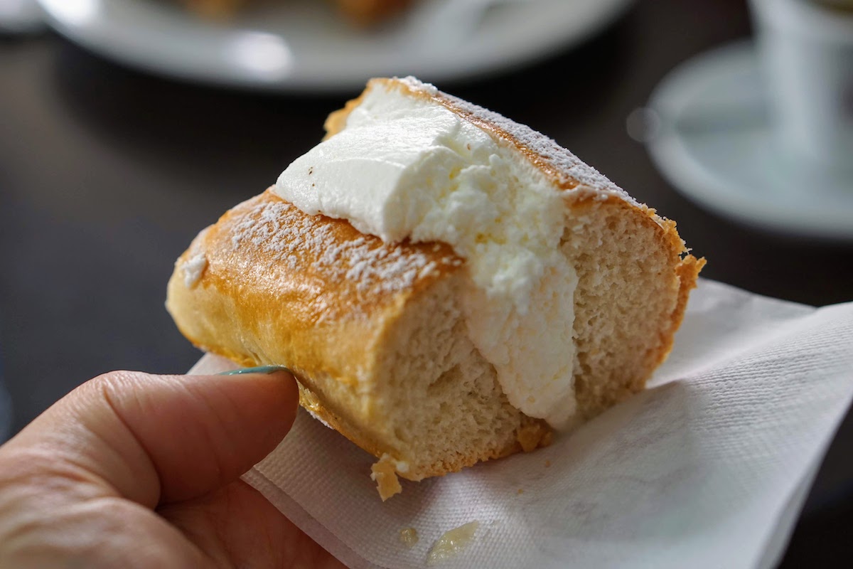 Close up of a person's hand holding a pastry stuffed with whipped cream