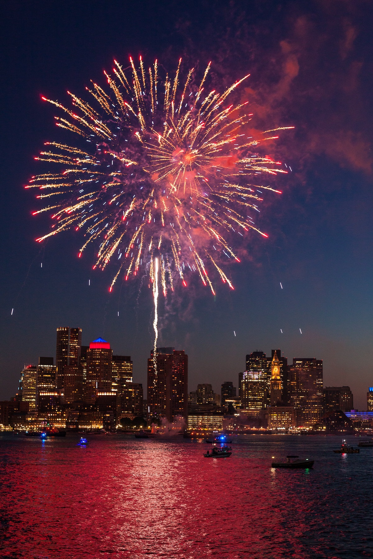 A huge red and white firework explodes over the Boston skyline on the Fourth of July, one of the most fun Festivals in Boston