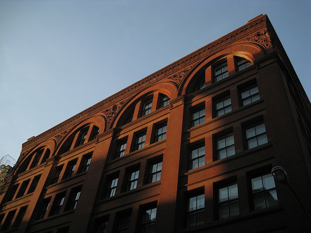 Sun setting on a tall brick building with many windows and columns