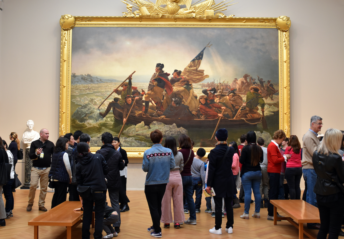 Crowd of people looking at a large framed painting of Washington crossing the Delaware River at the Met museum in NYC