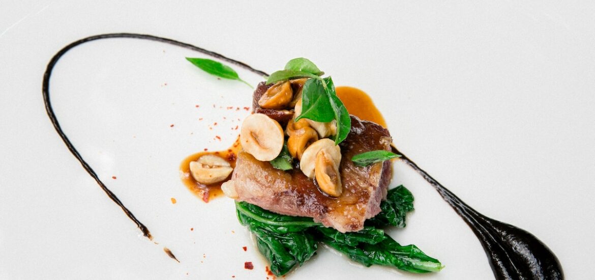 Modern presentation of a meat, vegetable, and nut dish served in a small portion on a white plate