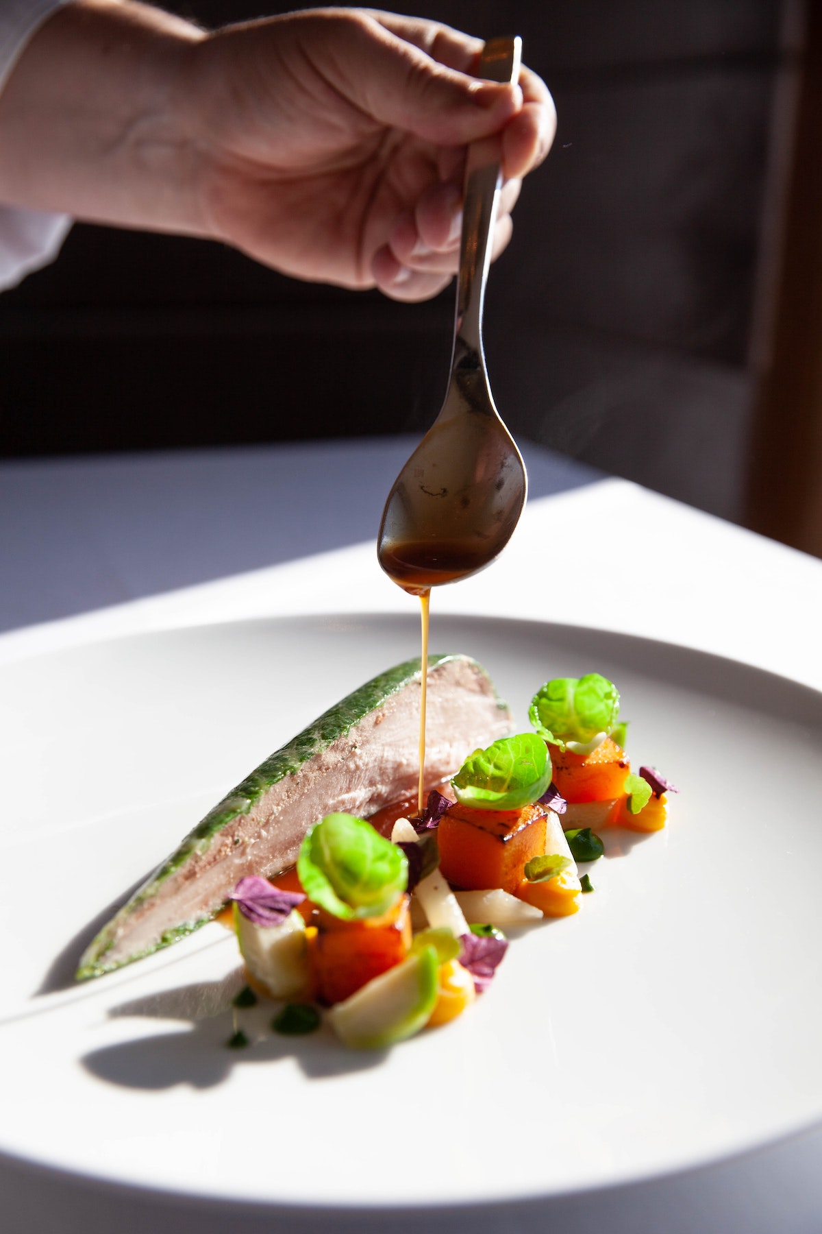 Sauce being spooned over artfully presented fish and vegetables on a white plate