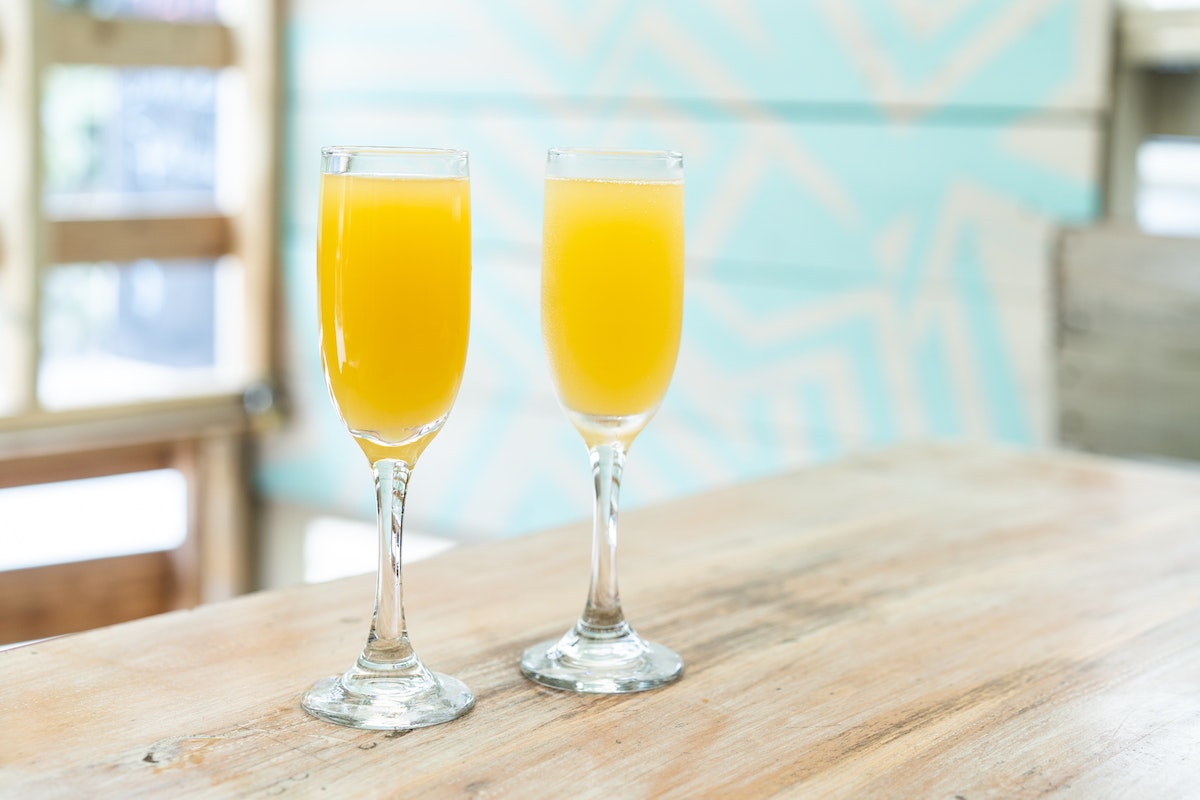 Two mimosas served in champagne flutes on a wooden table