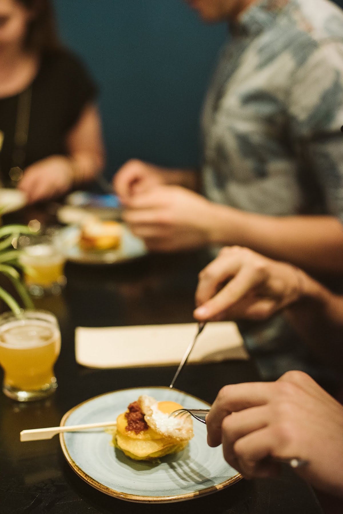 Person's hands cutting into a dish of eggs, sausage, and potatoes.