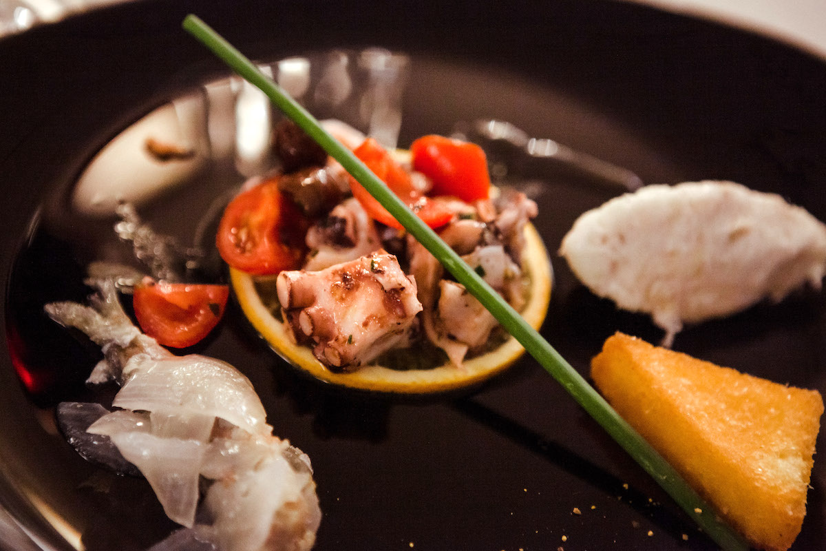 Modern presentation of an octopus and vegetable dish served on a black plate