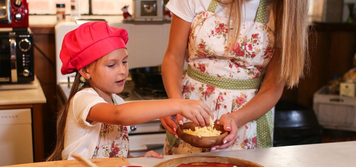 A woman and a young girl making a pizza at a white countertop