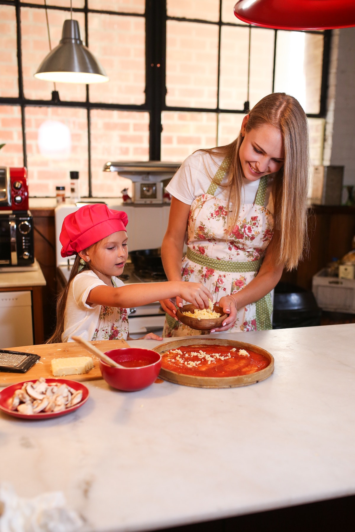 A woman and a young girl making a pizza at a white countertop