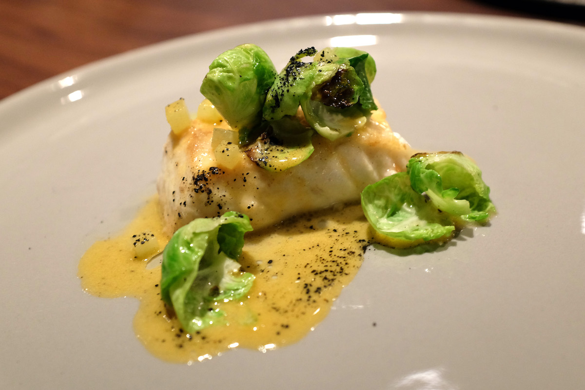 Halibut with brussels sprouts served over a bed of yellow sauce