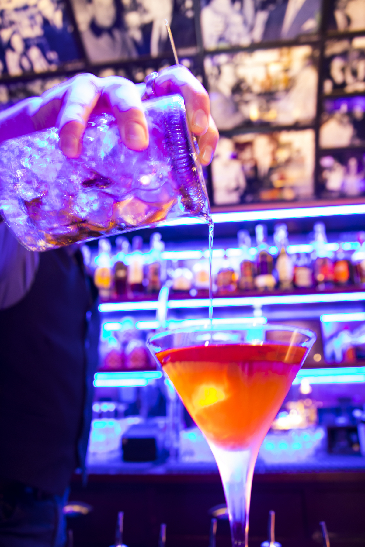 Close up of a bartender making an orange-colored cocktail.