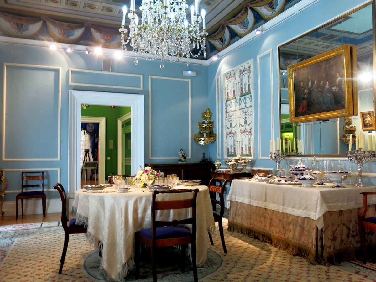 Interior of an old-fashioned dining room with light blue walls and a crystal chandelier above the table.
