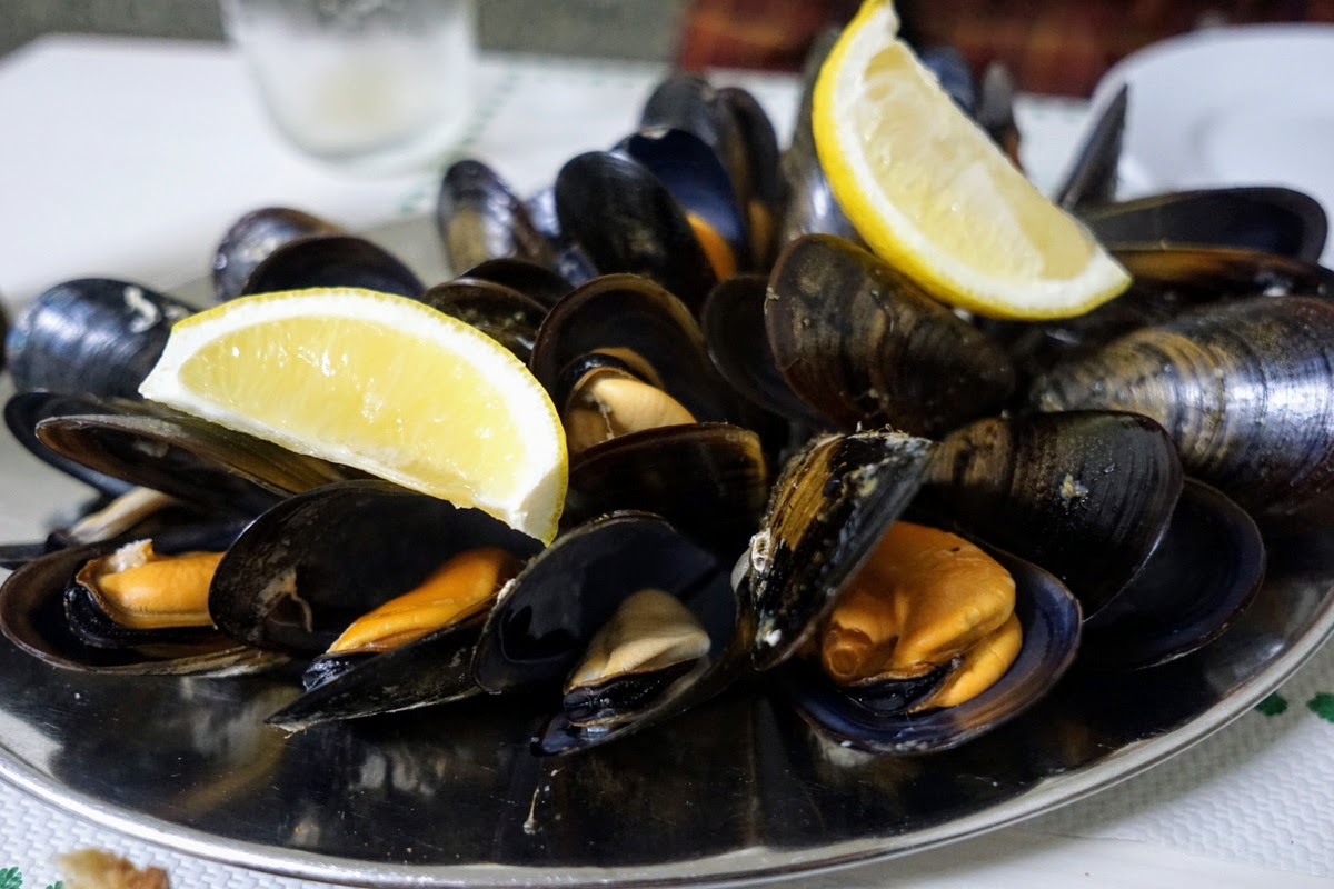 Close up of a plate of mussels with lemon wedges.