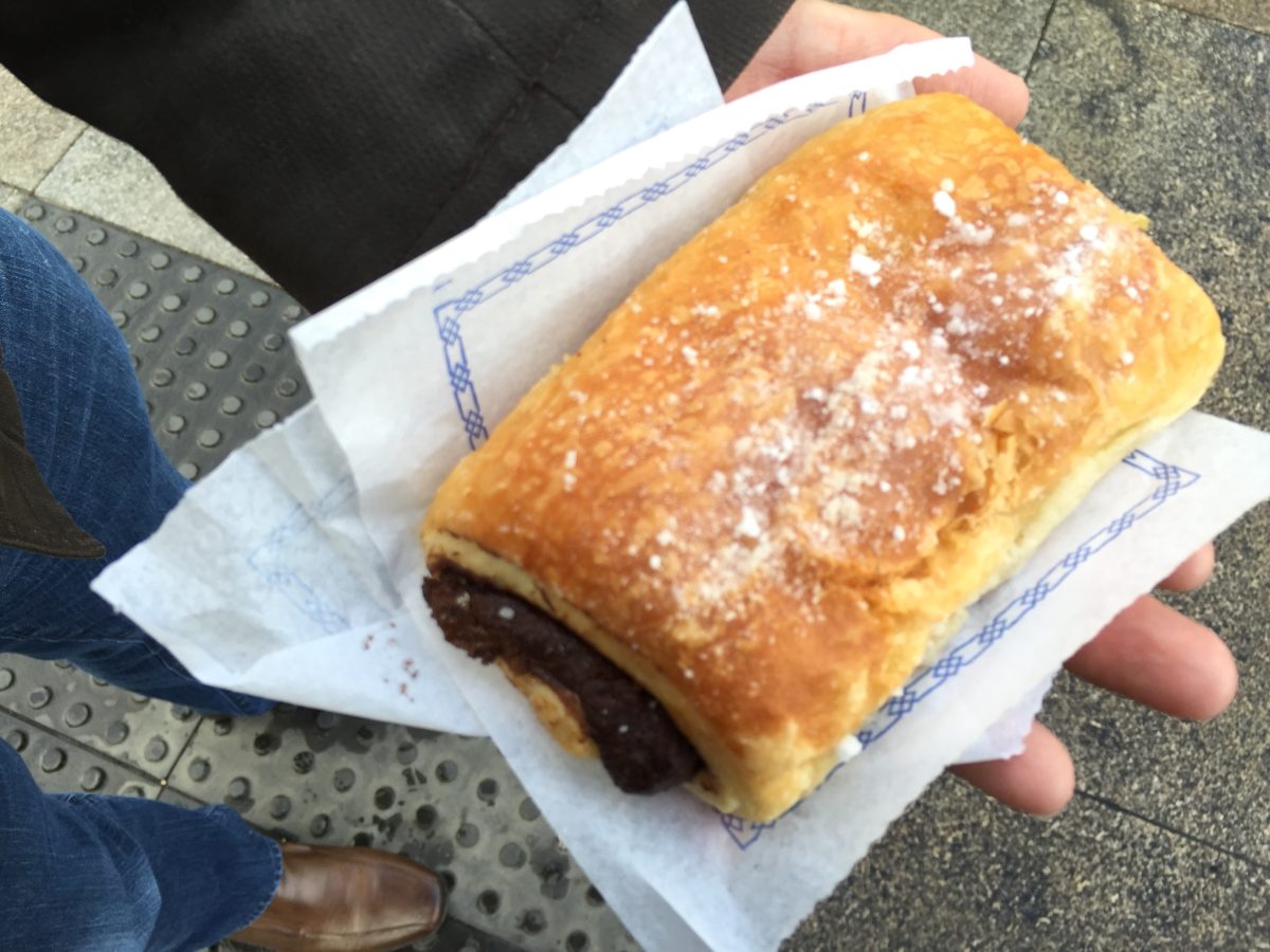 Chocolate-stuffed pastry dusted with powdered sugar on top of a white napkin in a person's hand.