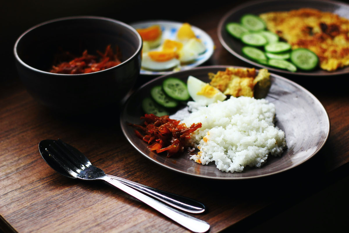 Several Malaysian dishes on a table with a plate of white rice and vegetables in the foreground.