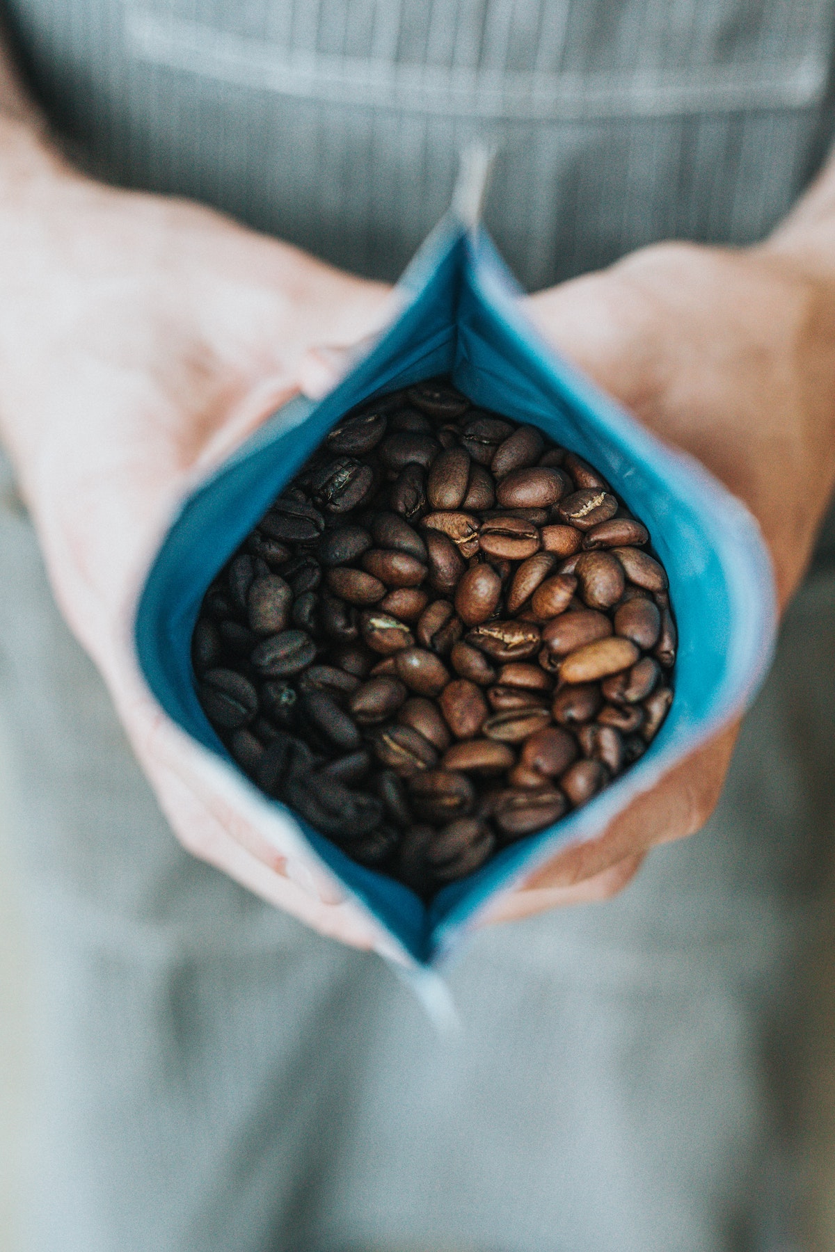 close up of a person holding open a blue bag of roasted coffee beans