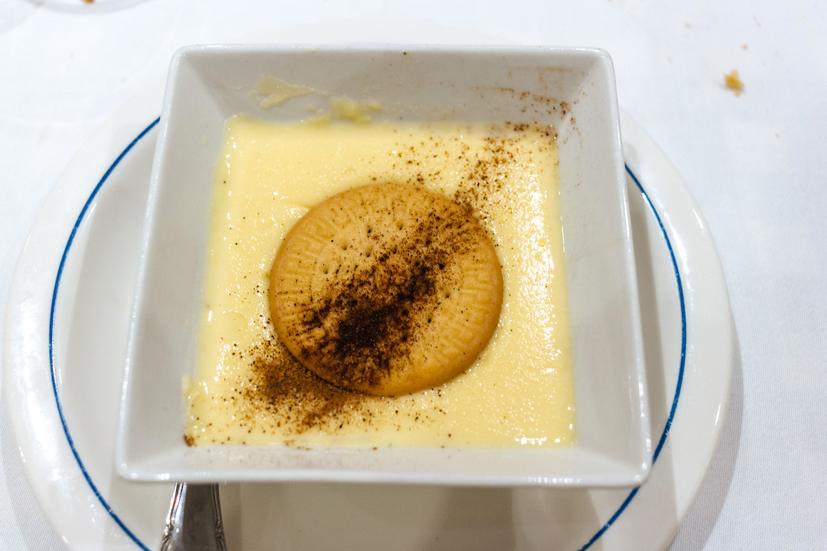 Spanish custard dessert in a square-shaped dish topped with a cookie and a dash of cinnamon