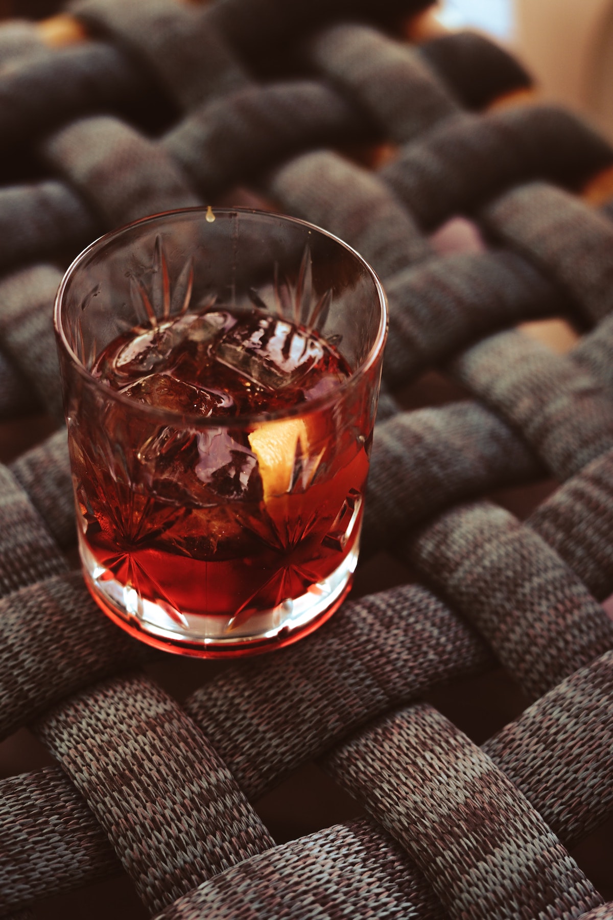 Brown cocktail in a short glass atop a woven black surface.