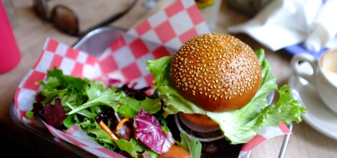 Traditional burger on a sesame seed bun with salad served in a metal tray with red and white checkered napkins