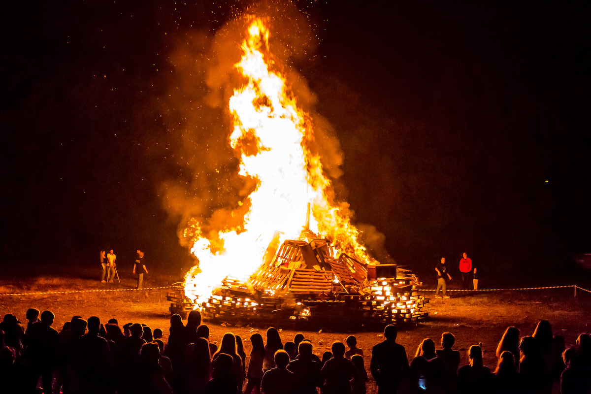 A large bonfire burns while a group of people watches.