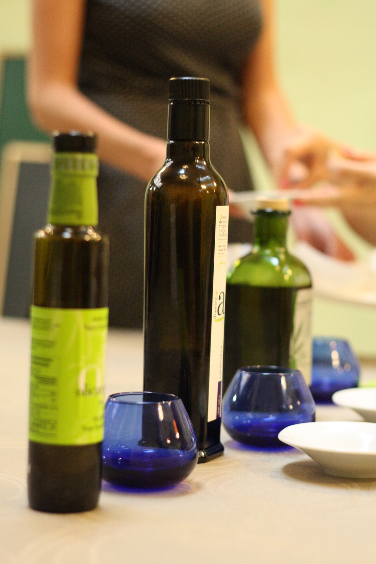Three bottles of olive oil next to blue tasting cups.