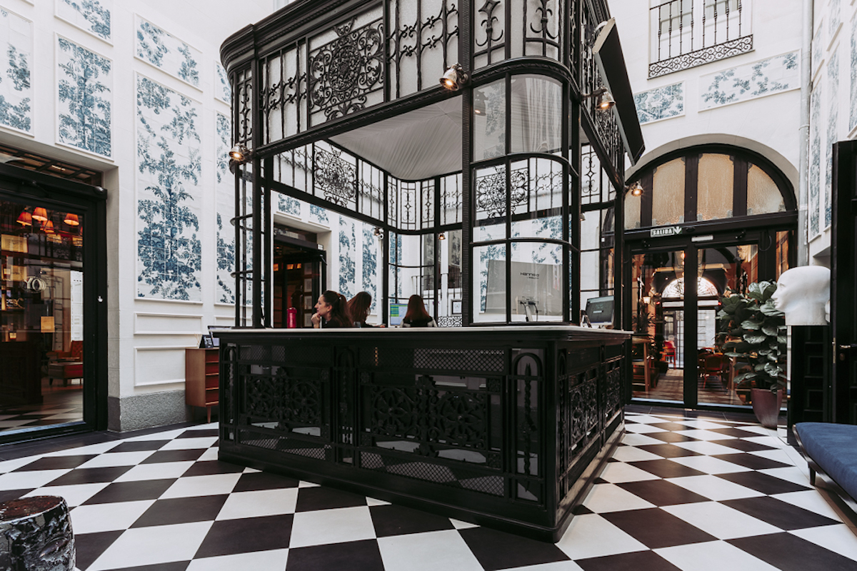 Hotel lobby with black and white checkered floor and an ornate wrought iron front desk. 
