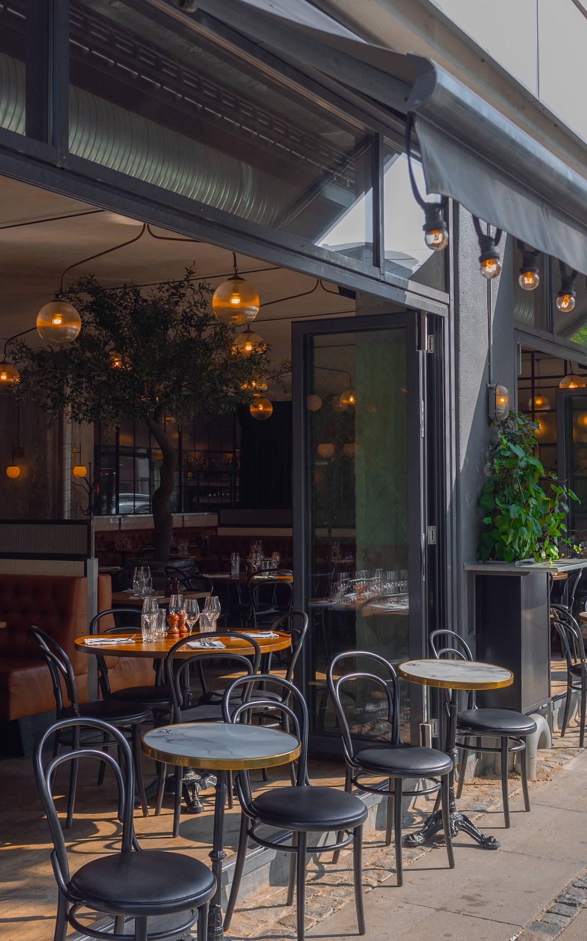 Sidewalk terrace at a cafe with small black tables and chairs.