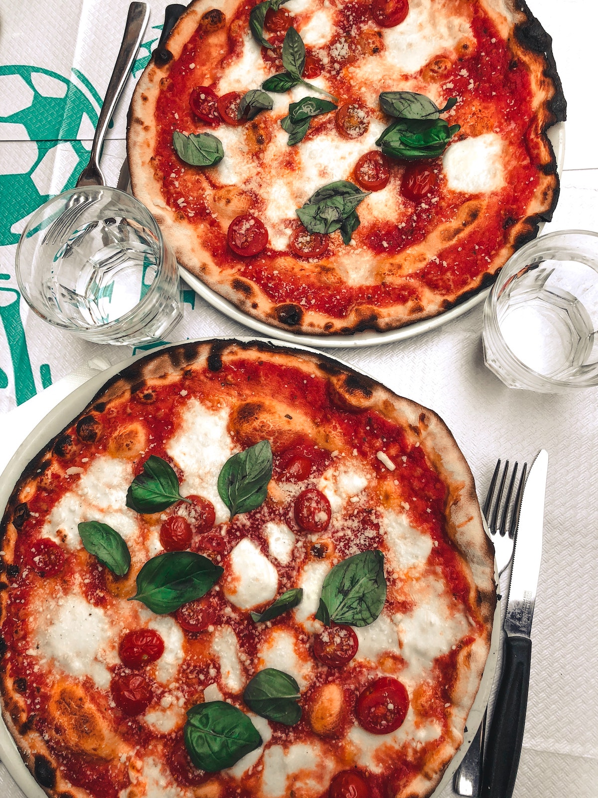 Overhead shot of two whole margherita pizzas with tomato, basil, and mozzarella cheese