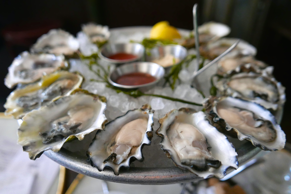 Round silver tray of oysters served over ice with various sauces in the center
