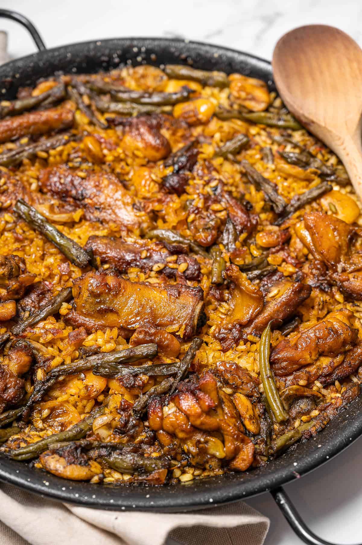Paella Valenciana with chicken, ribs, and green beans. A traditional Spanish meat paella with a wooden spoon resting on top.