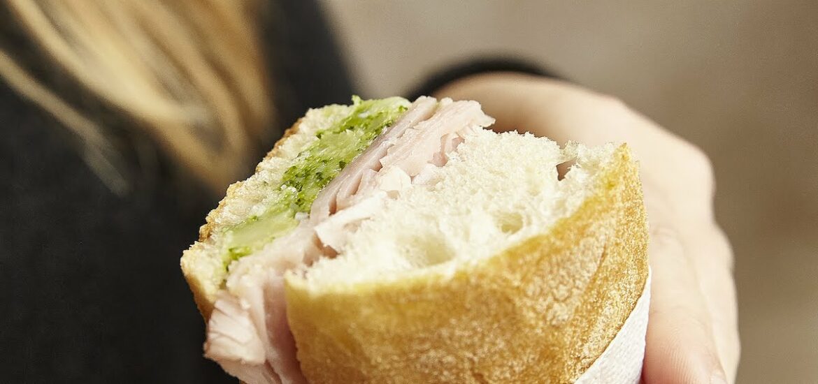 Close up of a person holding a small sandwich with prosciutto and broccoli