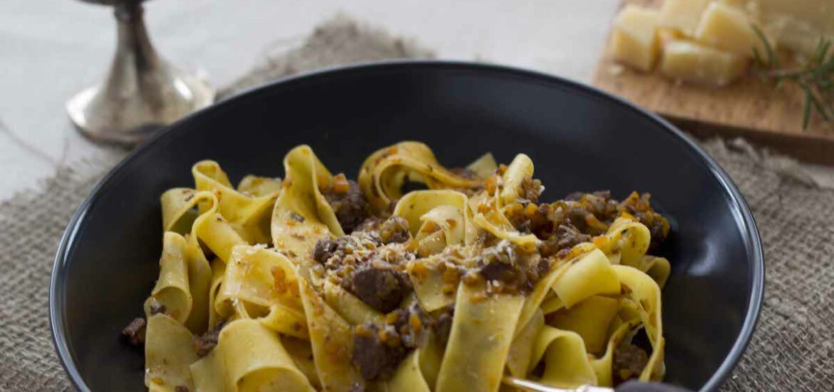 Wide pasta noodles with wild boar ragu on a black plate