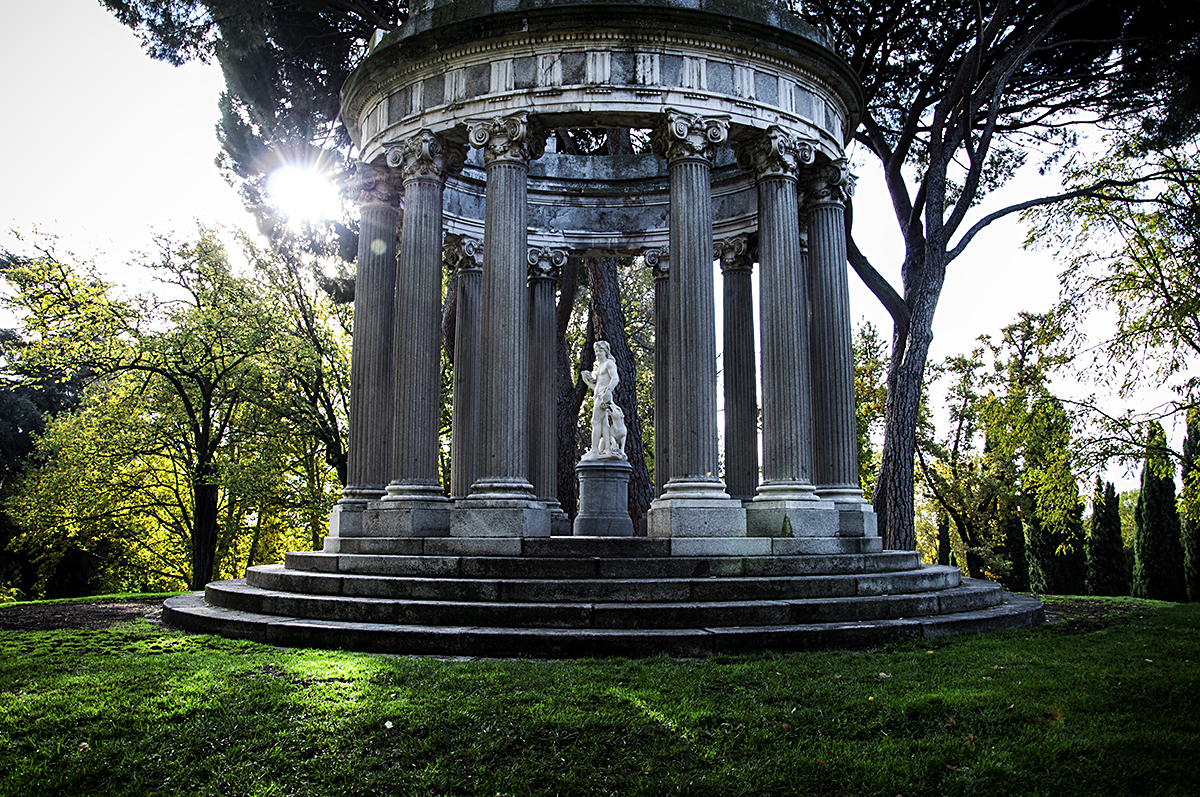 Round pavilion in a park decorated with columns with a statue in the center.
