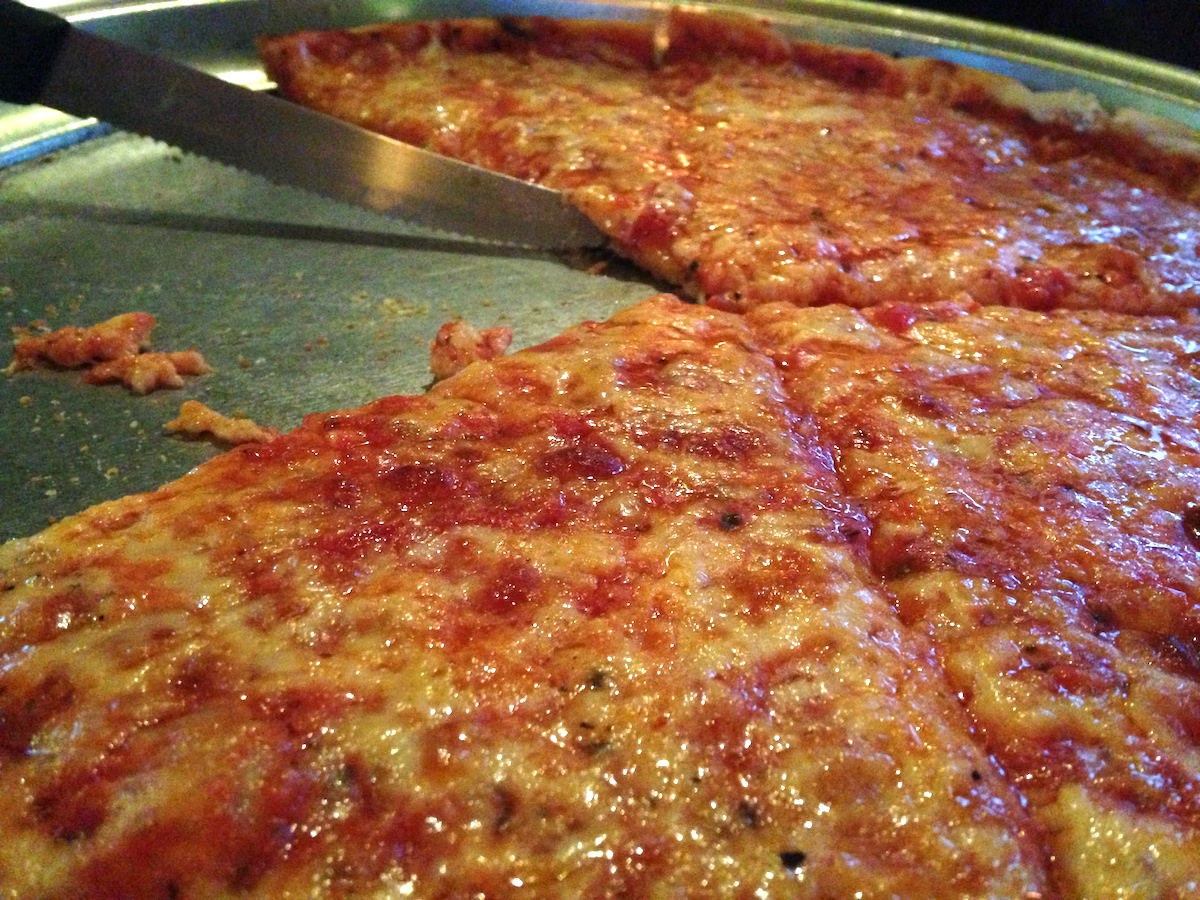 Close up of pizza cut into individual slices on a metal serving pan