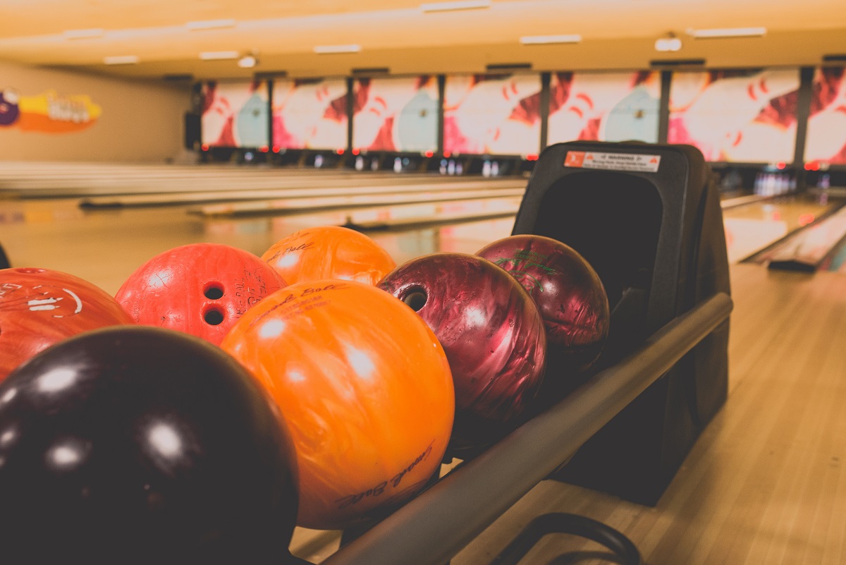 Orange and purple bowling balls lined up on a rack in front of a bowling lanes