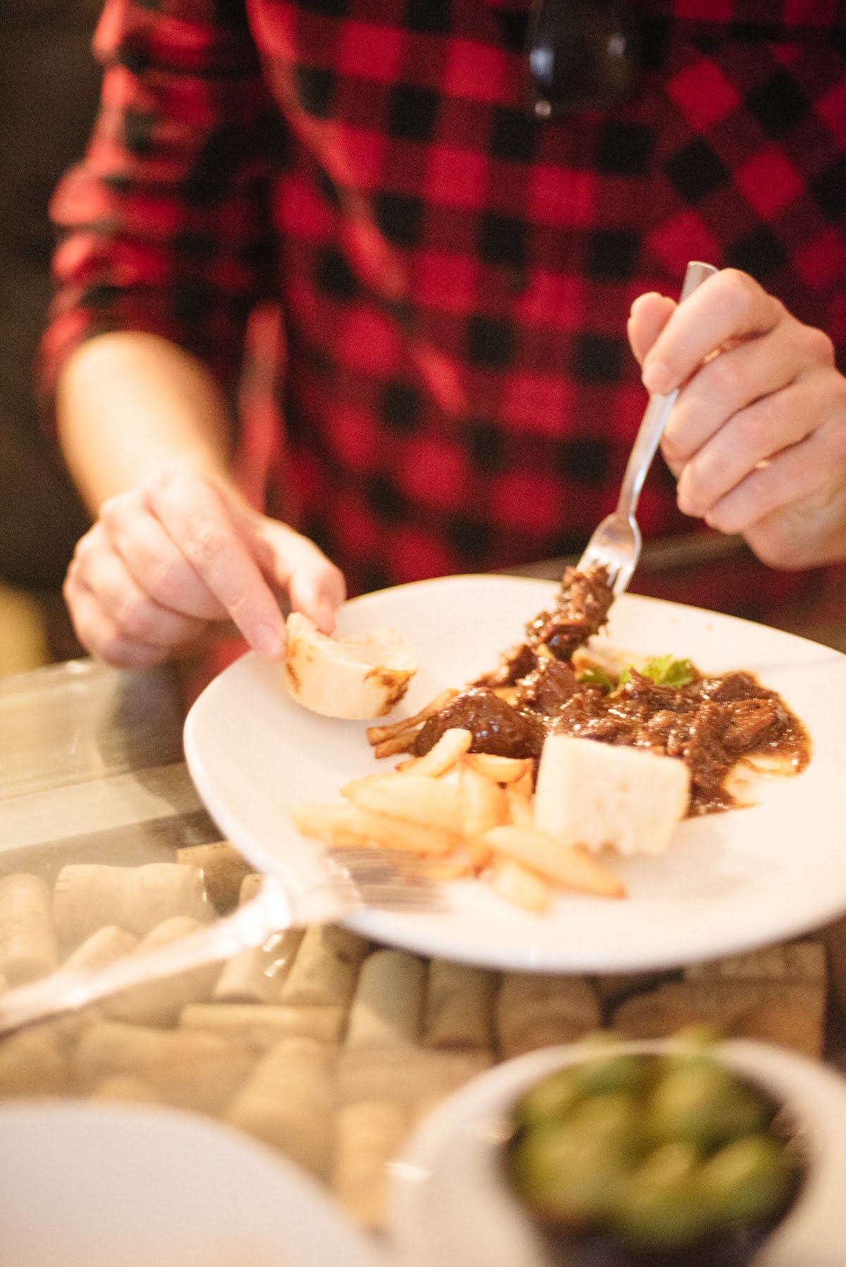 Close up of a person in a red shirt eating a meat dish while using a piece of bread to soak up the sauce.