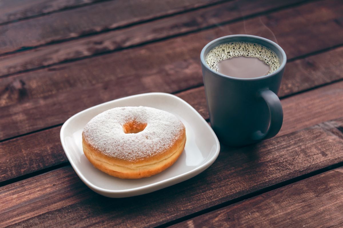 doughnut-on-white-ceramic-plate-beside-ceramic-mug-on-brown-wooden-table