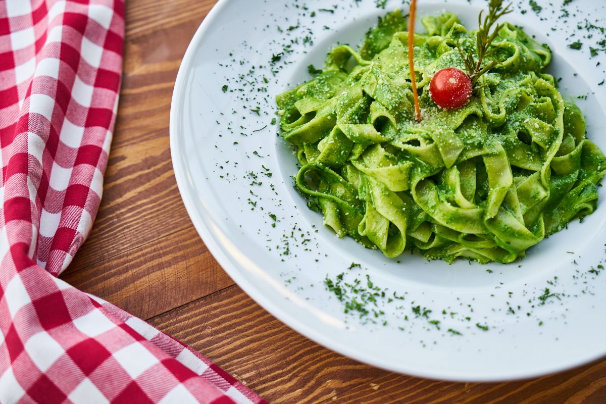 green pasta in white plate next to checkered towel
