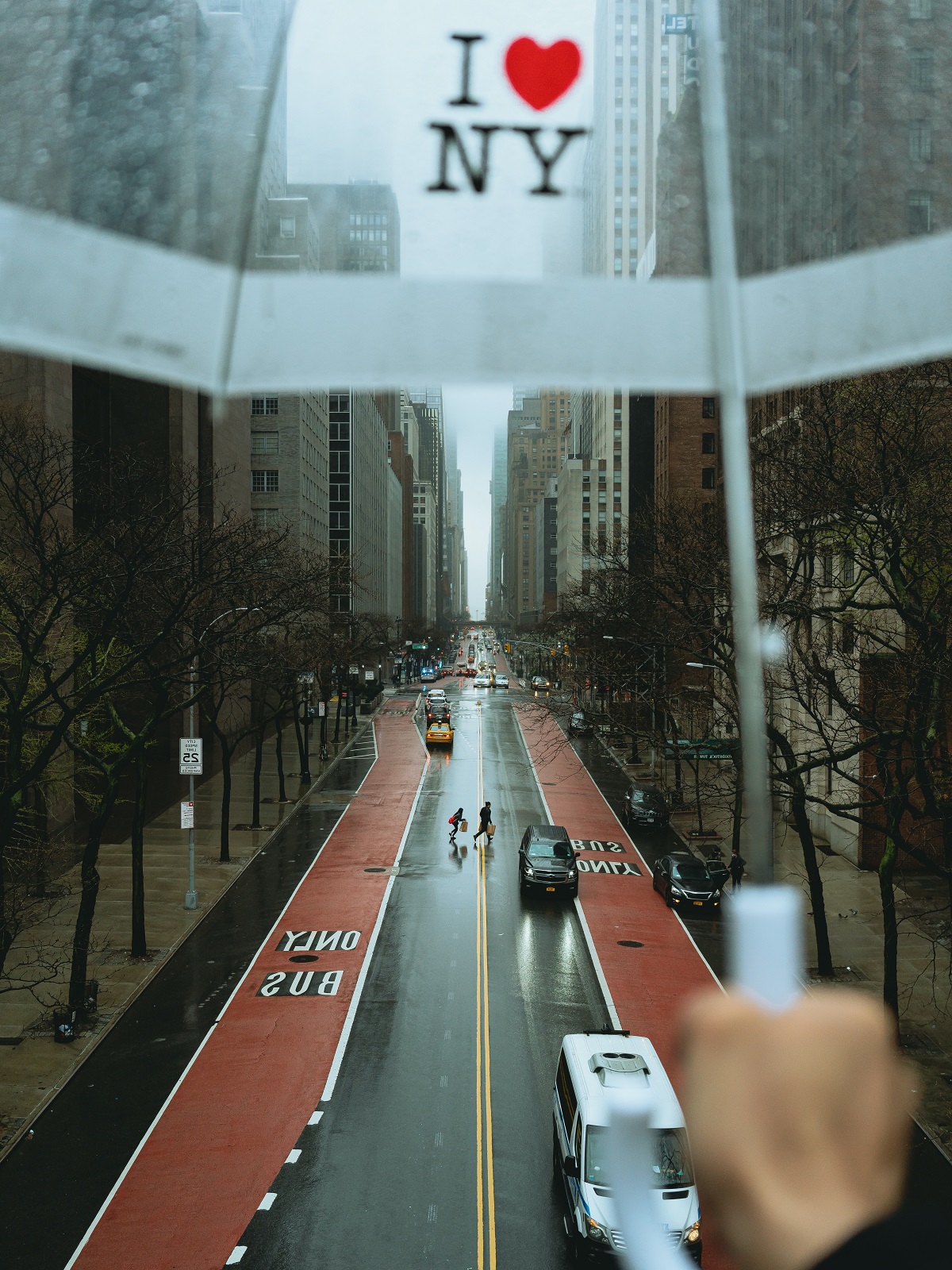 Person holds up a clear umbrella that says "I love NY" above a rainy urban landscape