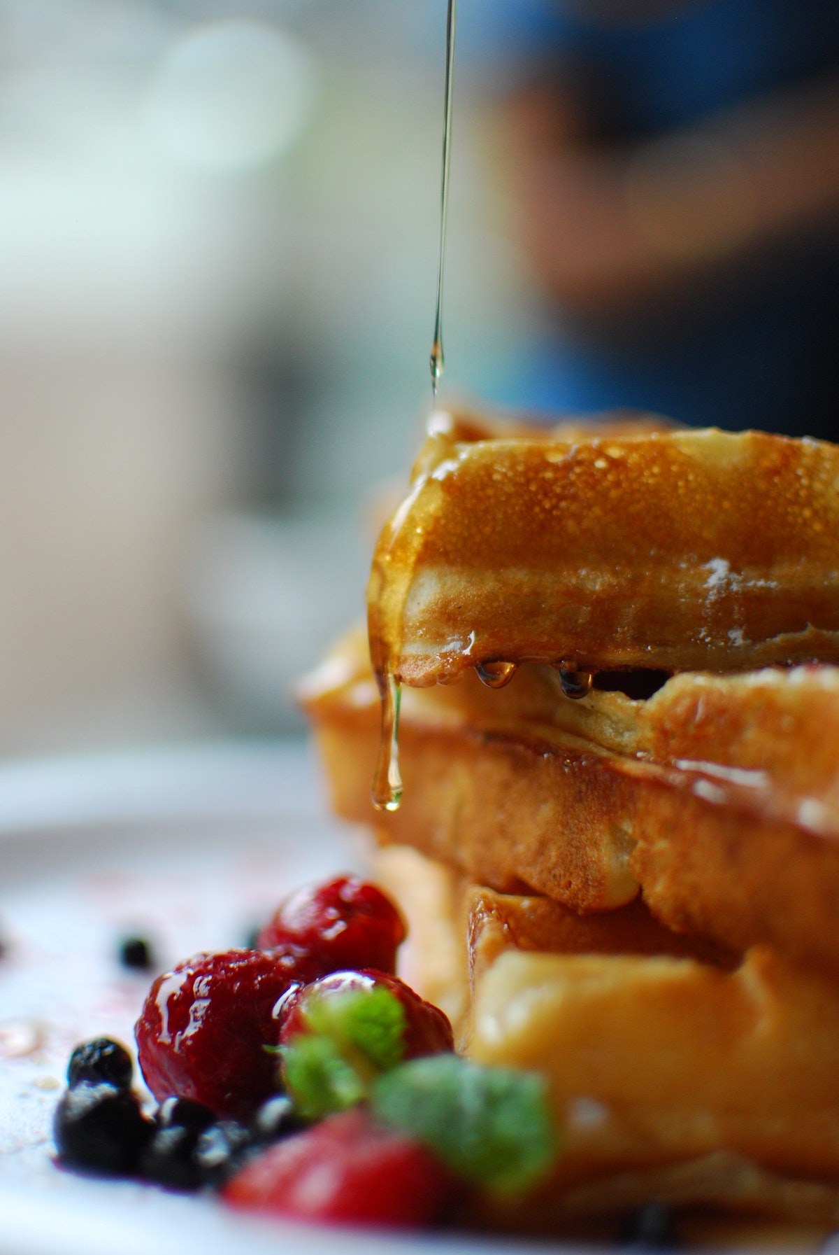 extreme close up of syrup being drizzled over a stack of three waffles with berries on the side