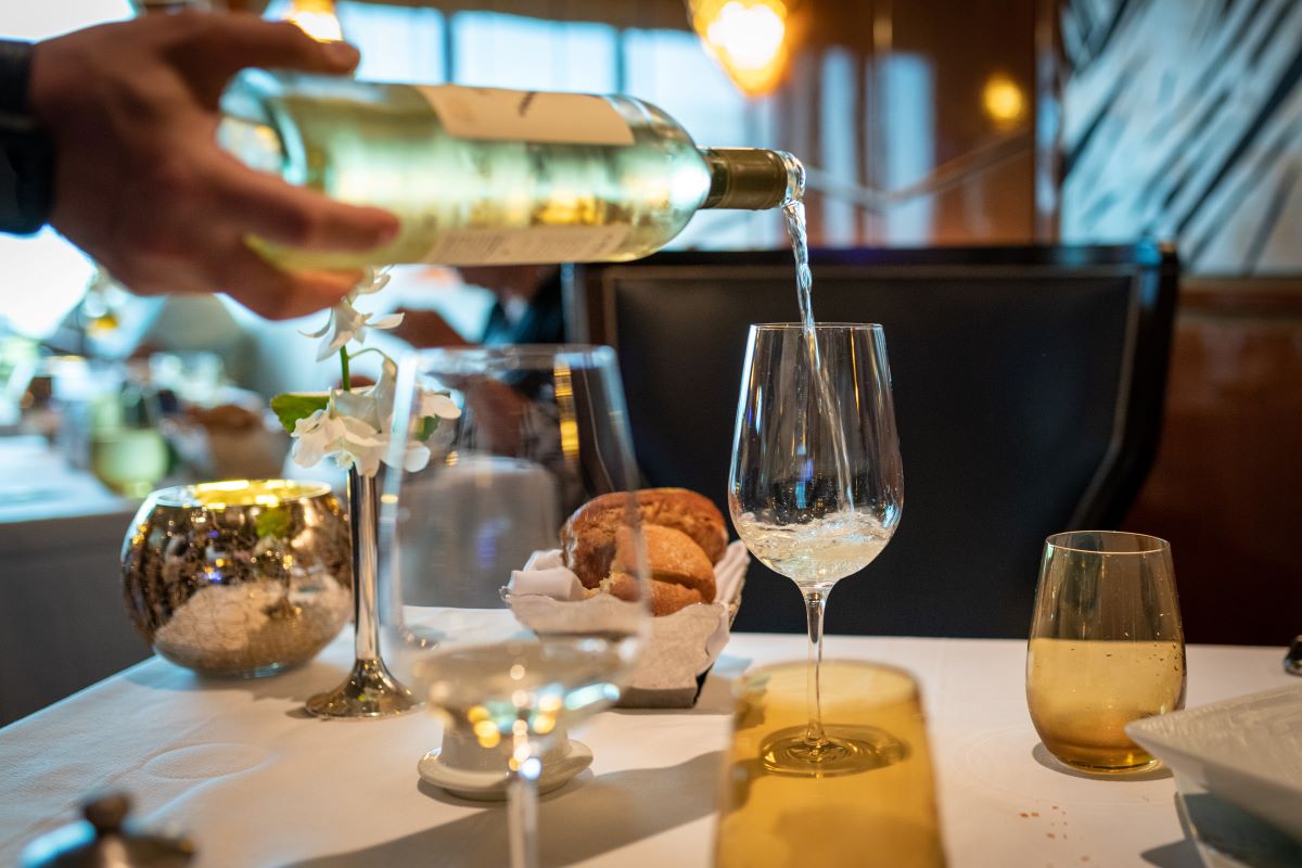 man pouring white wine into glass at a table