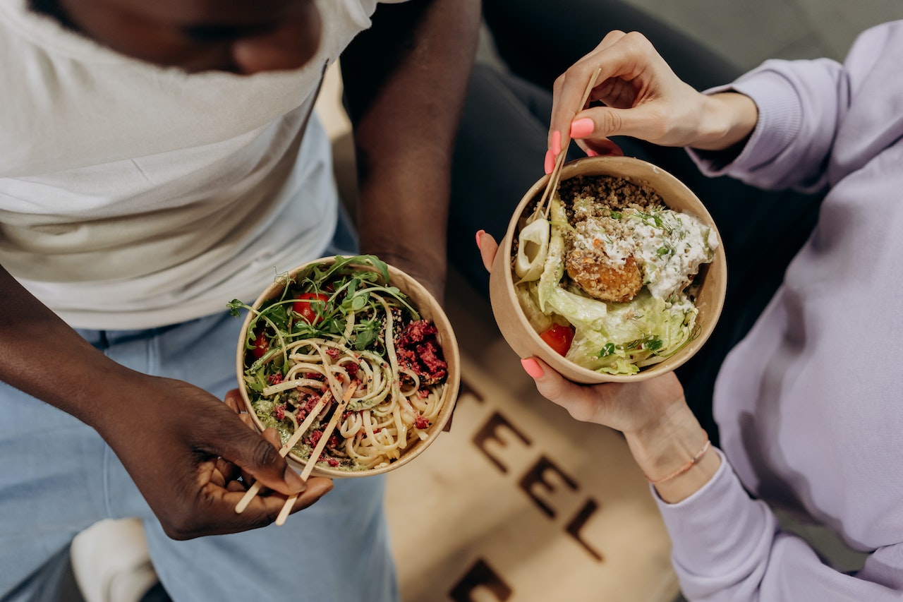 Two people eating salad and pasta in takeaway containers
