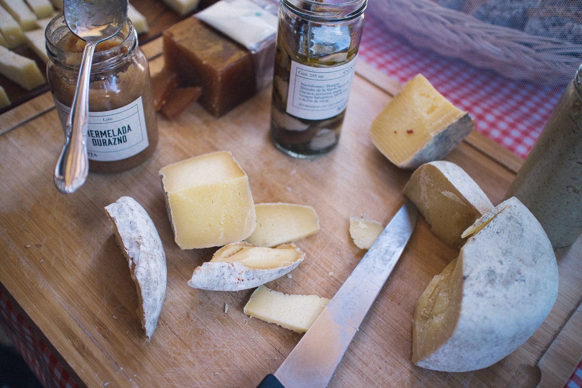 Wooden cheese board from above with multiple cheeses, jam, and a knite