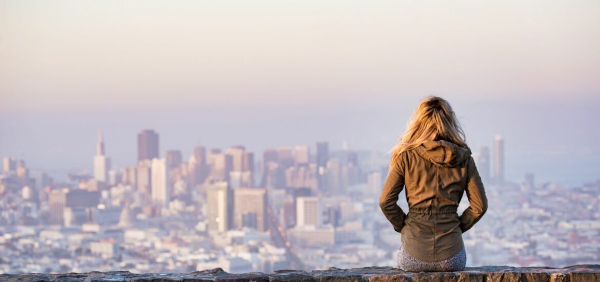 woman sitting on stone wall overlooking new york skyline