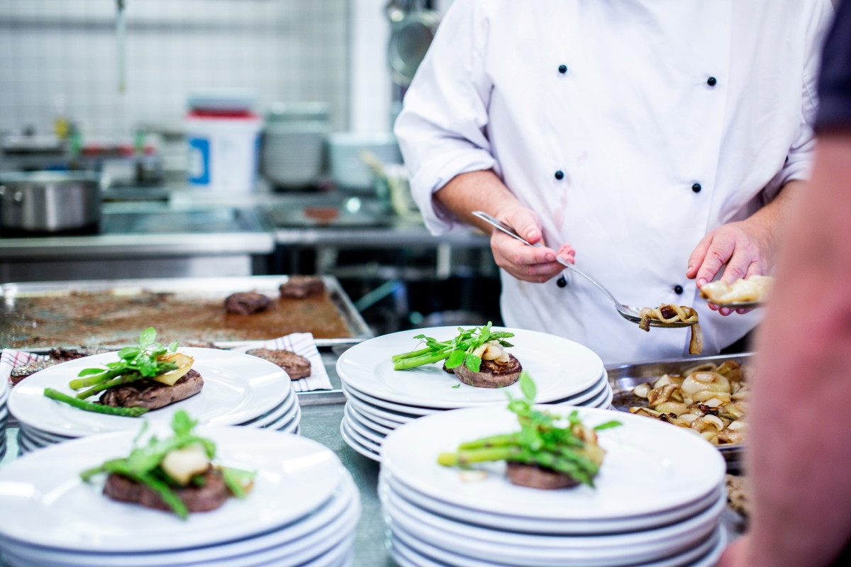 chef in white jacket plating food on white ceramic plates