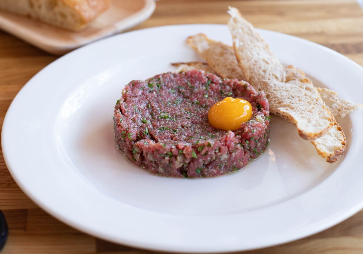 beef tartare on white plate with egg yolk and toast