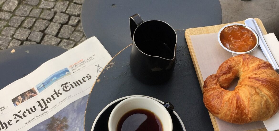 Croissant and a black coffee at an outdoor table with the New York Times newspaper