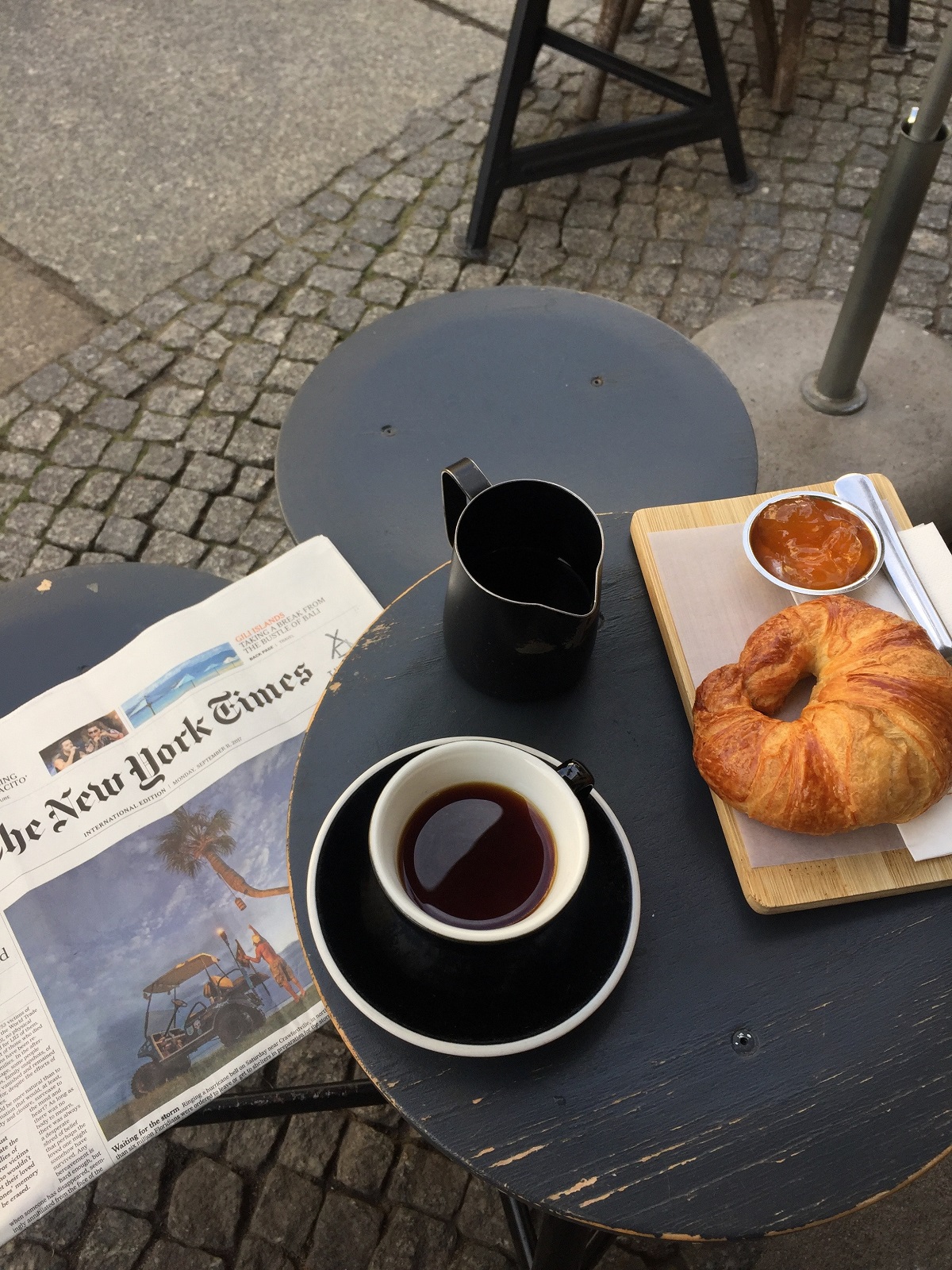 Croissant and a black coffee at an outdoor table with the New York Times newspaper
